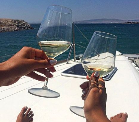 Hands holding wine glasses on boat catamaran cruise tour in Athens Greece with Sailing Athens. Complimentary wine on boat.